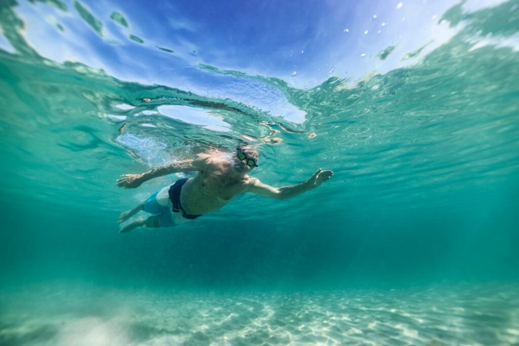 Senior man enjoying swimming underwater in clean, shallow sea